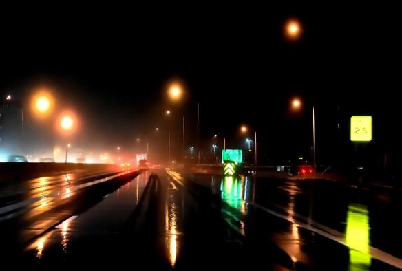 On a dark night, street lights reflect off the rain soaked highway.