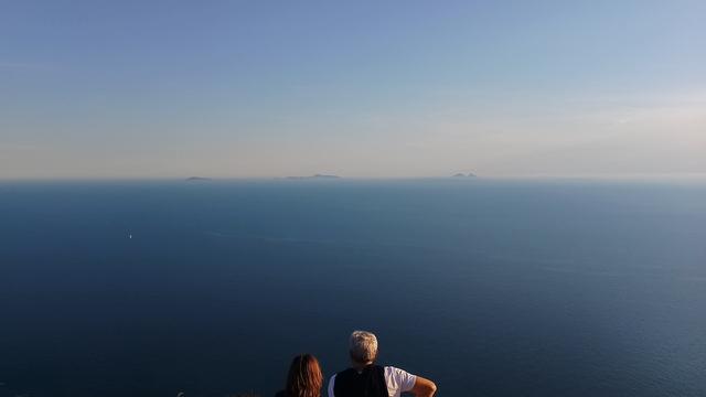 a couple looking at the sea with three islands in the distance