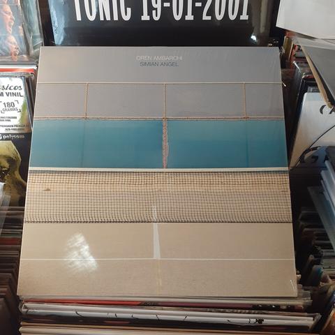 Album cover features detail of a tennis court. The court is grey in color, and a shade cloth attached to a chain link fence in the background is aqua blue. The lines of the court, net, and fence combine to create a grid-like pattern.