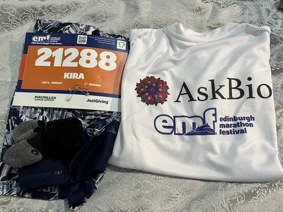 Running kit (blue patterned leggings, black socks, white y-shirt printed with AskBio and EMF logos) and number (21288 Kira) laid out ready.