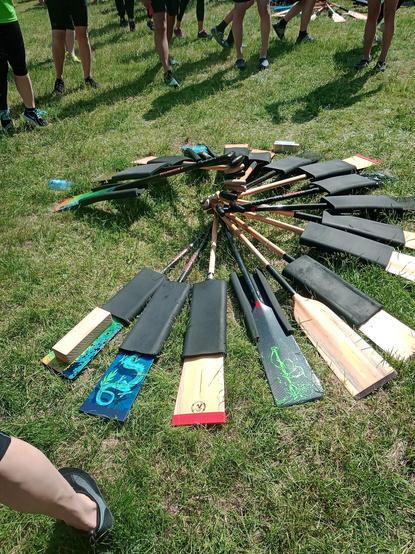 22 Paddel liegen auf einer Wiese zu einem Kreis gelegt, die Enden aufeinander