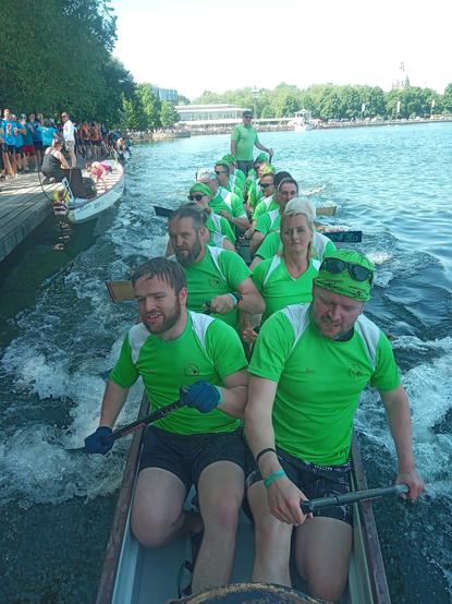 Ein Drachenboot, voll besetzt, die Paddler/innen bremsen das am Steg
Die Gesichter sind freudig