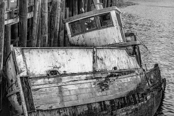 Sunken Boat In Noyo Harbor B and W II

This is an image of an old fishing boat that sat tied to the docks for years. Finally during a strong North Coast winter storm the hull failed and the boat sank in Noyo Harbor. 
The paint, where there is some, is peeling off. Planks are missing from the bow, and barnacles are growing on the side of the boat. They must attach themselves when the tide is high.