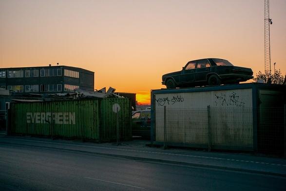 Sunset behind a Scrap yard, seen between two containers. On top of one of them an old car