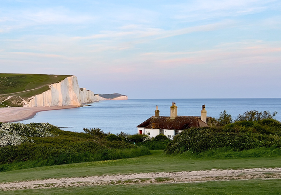 View of white cliffs at Beachy Head with a cottage in the foreground.