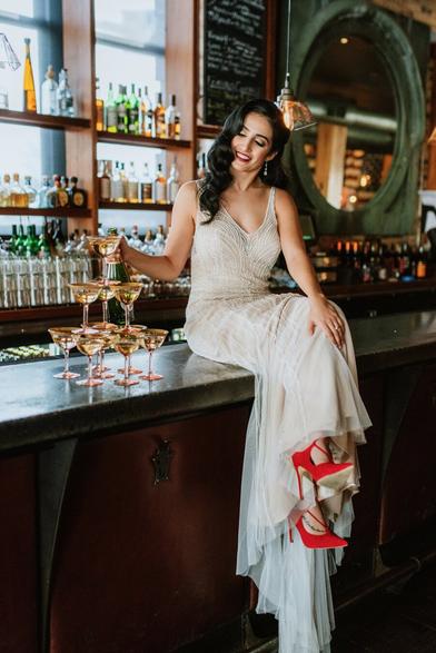 Bride sits on bar pouring champagne