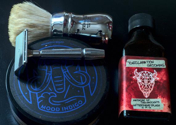 A chrome GEM Micromatic Flying Wing on a tub of House of Mammoth Mood Indigo next to a bottle of Declaration Grooming Massacre of the Innocent splash and a Zenith B21 brush