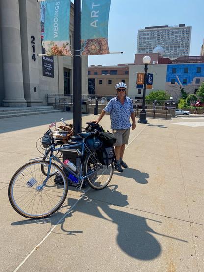 An old man stands next to his old bicycle; a newer bicycle is in the foreground. The background is Union Depot in St. Paul. The cyclists have completed a cycling tour; one will board the Amtrak here, and the other will board light rail to Minneapolis then commuter rail to Anoka County, thus completing the tour.