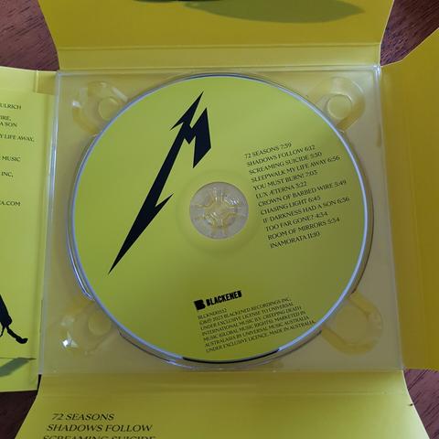 New Metallica album 72 Seasons, with the four sides folded out to reveal a yellow CD inside, featuring a stylised M lightning bolt band logo and the track list for the album.