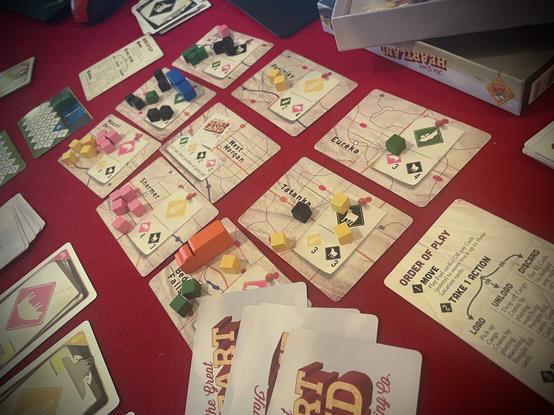 Game components for The Great Heartland Hauling Co. Primarily a highway map of the USA made up of nine cards. Also wooden cubes and little semi-trucks. On a red velvet background.