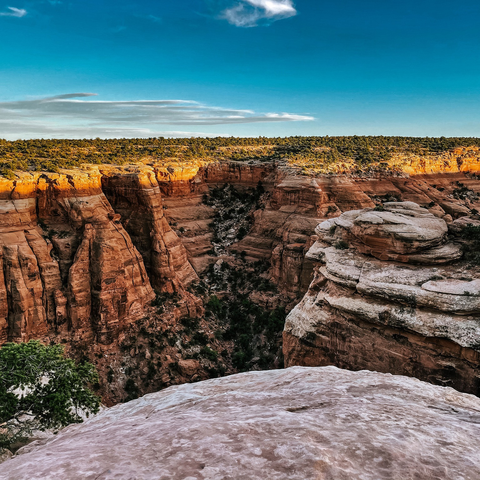 Redrock canyons turning orange in the setting sun, with a blue sky and a few clouds above.