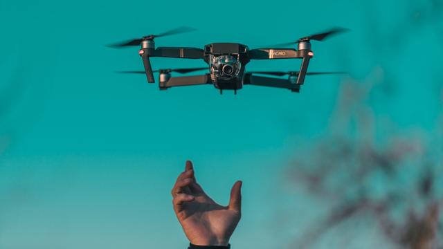 In an open area, a camera drone is released to fly from the hand of a cinematographer.