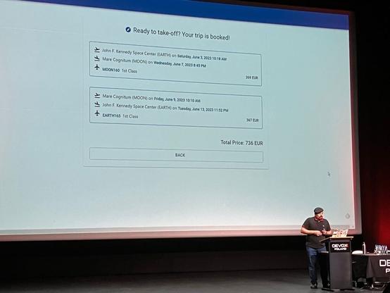 Julien demonstrating a booking confirmation page in his example app. It says a round-trip from John F. Kennedy Space Center (EARTH) to Mare Cognitum (MOON) costs 736 euros.