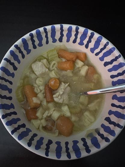 Chicken noodle soup in a blue and white ceramic bowl.