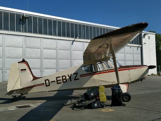 Flugzeug vor Halle mit Fahrrad und vielen großen Taschen.