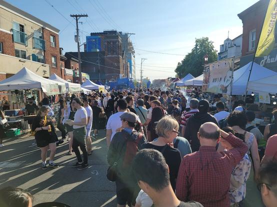 Large crowd of people waiting in line for tent booths lining a city street