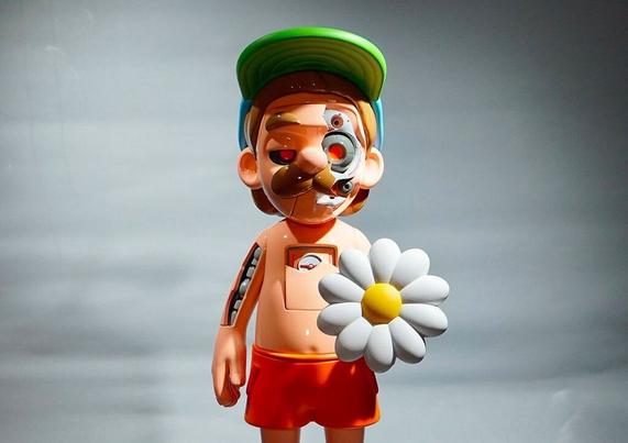 An art toy by tOBEY Toy featuring a moustachioed character wearing a coloful cap and orange shorts. The character is holding a large white daisy. A piece has been detached from his face, revealing a robotic structure.