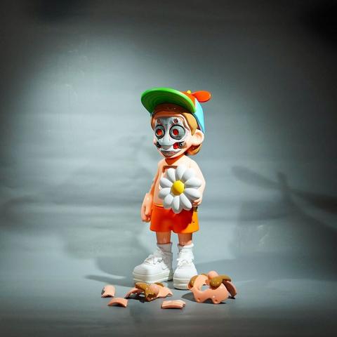 An art toy by tOBEY Toy featuring a moustachioed character wearing a coloful cap, orange shorts and white sneakers. The character is holding a large white daisy. Pieces have been detached from his face, revealing a robotic structure.