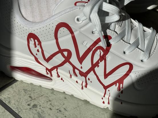 Foto zeigt weiße Sketchers-Turnschuhe mit drei blutenden Herzen.