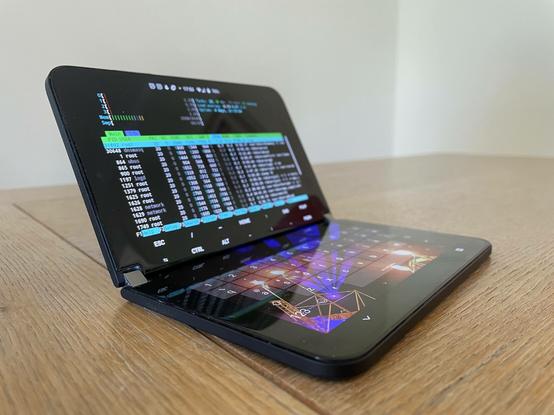 Surface Duo device in "clamshell" mode, with the top screen displaying htop output from an ssh session to a router and the bottom screen showing a virtual keyboard