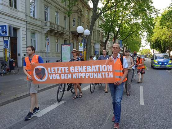 Demonstrationszug mit Demonstranten und Demonstrantinnen der Letzten Generation, vorn mit Spruchband, Text:"Letzte Generation vor den Kipppunkten".