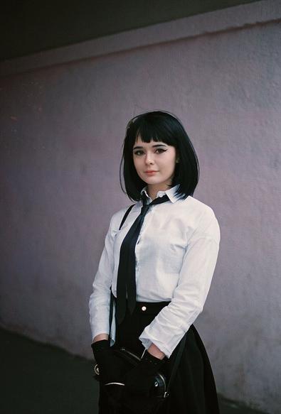 A girl cosplaying Yosano Akiko from “Bungou Stray Dogs”. She's wearing white blouse, black skirt and black tie.
