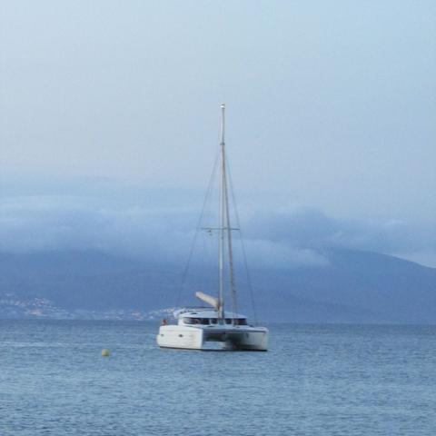 Catamarán a l'aigua amb les muntanyes del cap de creus Alfons amb els pics coberts de núvols