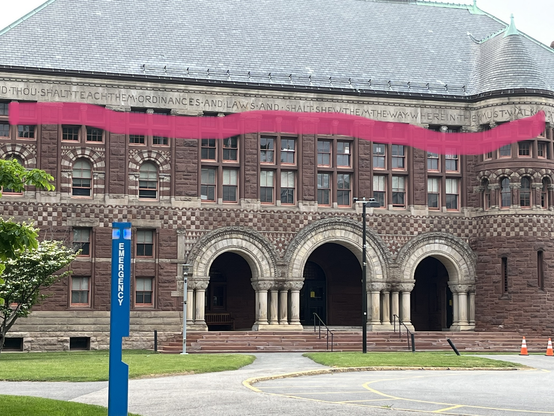 Image shows a brown building that says “thou shalt teach them ordinances and laws and shalt shew them the way wherein they must walk… and they must do.” Building is on the campus of Harvard law school
