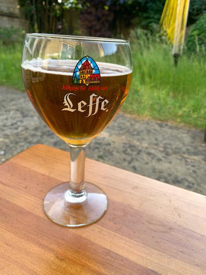A glass of Leffe Blond beer on a table with a garden in the background.
