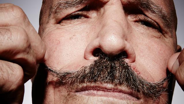 A man's face fills the frame. His mustache is beautiful.