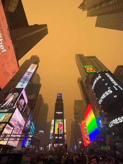 Times Square blanketed in the orange haze of wildfire smoke, neon signs clashing against the haze