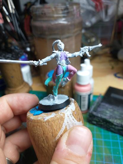 A partially painted harlequin from Warhammer 40k. Large patches are pastel green, purple and pink. Other parts are still grey
