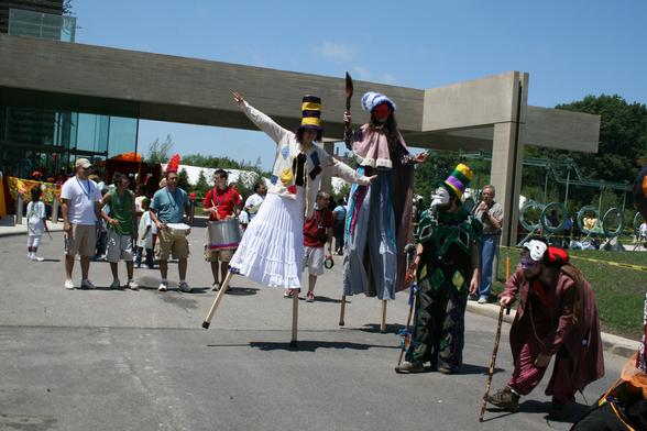 Four actors (including two on stilts) in commedia dell'arte costumes and masks getting ready for an arts parade.