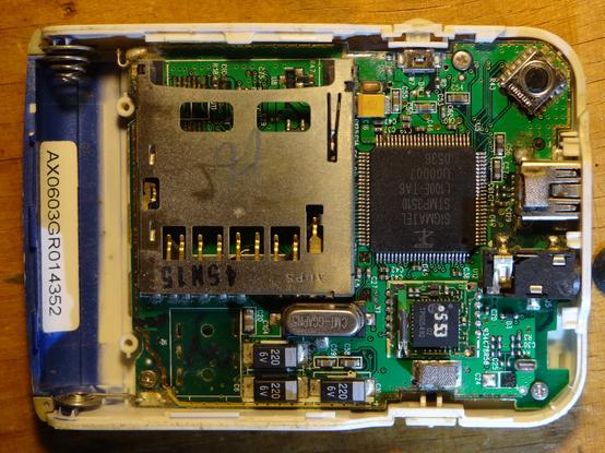 PCB still in its case.  There is a big SD card holder, AAA battery holder, a rotary encoder, microUSB port, SIGMATEL DSP chip, other small chip with "dot 5 53" painted on it, and a bunch more components.