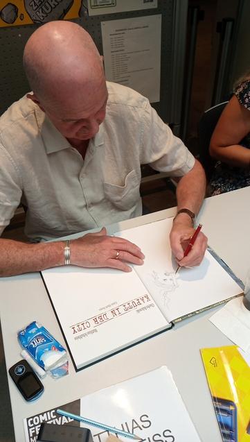 Matthias Schultheiss zeichnet mit Kugelschreiber eine Signatur in sein neues Buch "Kaputt in thr City".