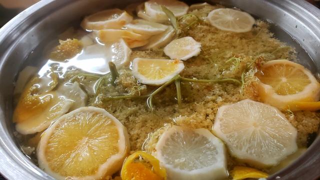 The cordial with the limes, lemons, and elderflowers steeping in a pot.