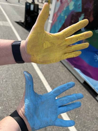 Two left hands with paint all over them from putting handprints on the Pride banner.