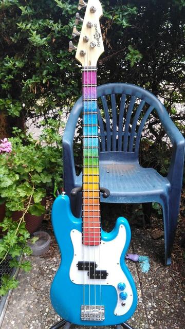 Blue short scale bass guitar with rainbow inlay stickers, and blue knobs that go to 11.