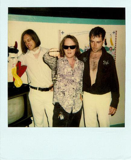 Polaroid photo of the band Urge Overkill after playing a headlining set at Jabberjaw in Los Angeles in 1991. King is wearing sunglasses. Nate is staring at a Devil Elvis head, and Blackie is unbuttoned and relaxing.