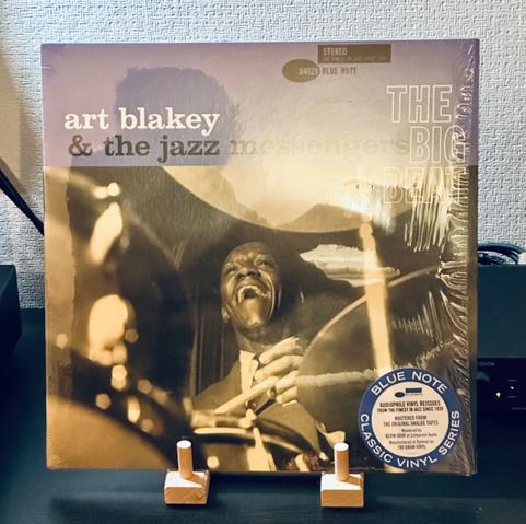 Photo of a record album jacket resting on a wooden stand. 

The record cover is a photograph of a grinning Art Blakey sat behind a drum kit, sticks in hand. 

A pale blue border runs across the top of the jacket where text reads, ‘Art Blakey and the Jazz Messengers, The Big Beat’.
