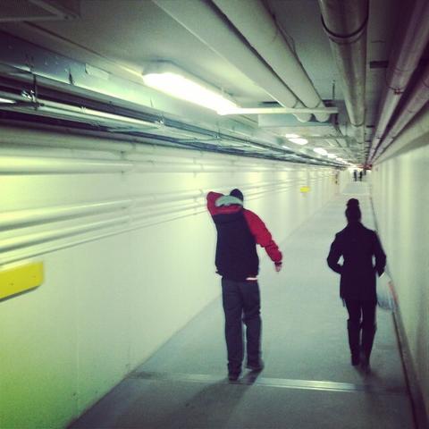 Two people walk into the distance; down a bright and stark underground tunnel.