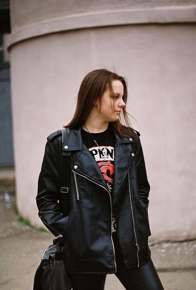 A girl with dark chestnut shoulder-length hair wearing leather jacket and pants and looking to her left