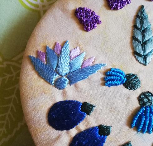 Close up of an embroidered piece inspired by the polychrome faience collars of ancient Egypt. The most prominent is a lotus flower. The embroidery is worked in silk, twisted by hand or used straight from the reel.