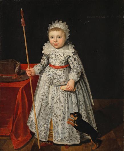 A young boy in a formal gown, dating 1630. The gown has a high, lace collar, and is made of blackwork embroidery (black thread in a floral motif on a white ground). He has a lace bonnet that looks like a crown, and a red belt. A dog is at his feet, and he carries a lance.