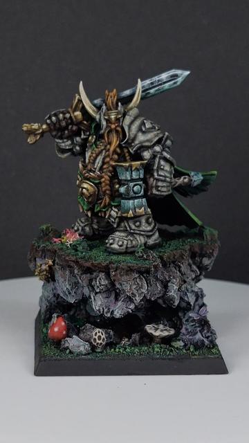 Dwarf paladin miniature standing on grassy outcrop with a small cave underneath wearing stone armour, carrying a sword and hammer with tiny insects and animals around