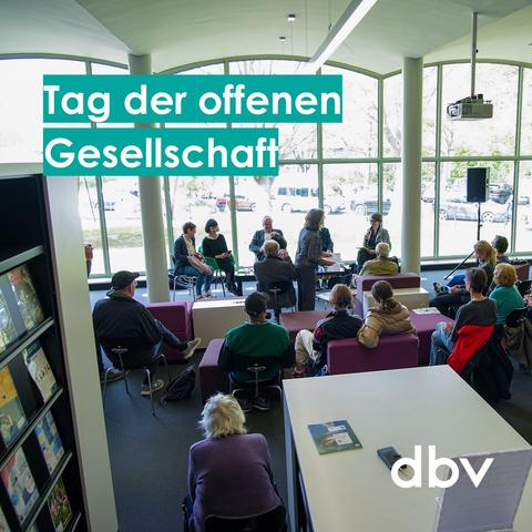 Auf dem Foto steht die Schrift "Tag der offenen Gesellschaft". Verschiedene Personen sitzen auf Sitzhockern in einer BIbliothek und hören einer Podiumsdiskussion zu. Im Vordergrund sieht man Regale mit Büchern.