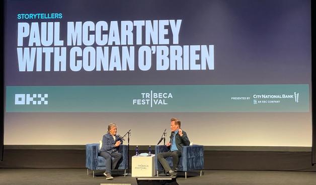 Paul McCartney and Conan O'Brien sit on blue velvet chairs next to microphones on stage at Tribeca Festival.