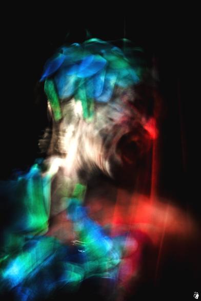 female self-portrait photograph (head and part of the upper body only) in bright colors, motion-blurred by long exposure and deliberate action.  the person, vaguely recognizable on a dark background, is dominated by green, turquoise and, above all, bright red around the wide open mouth, nose and throat, fiery, blazing.  her facial expressions also indicate the inflamed and her rage.