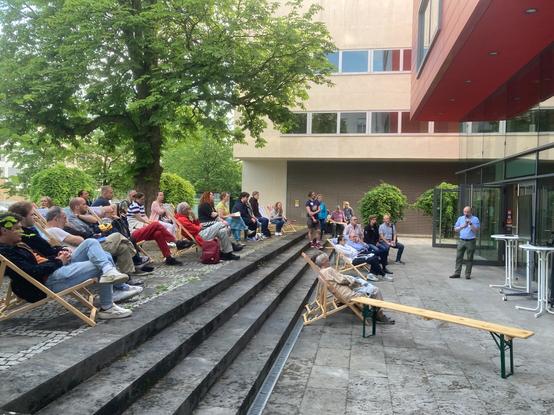 Scientist explains research to lay audience sitting on deck chairs