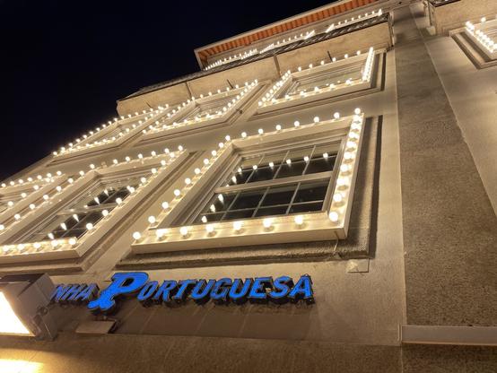 Fachadas de edifício comercial de 4 andares no Porto, à noite, com 28 janelas, cada uma circundada por 32 lâmpadas LED ligadas. O edifício destaca-se dos restantes pelo intenso brilho e poluição luminosa.